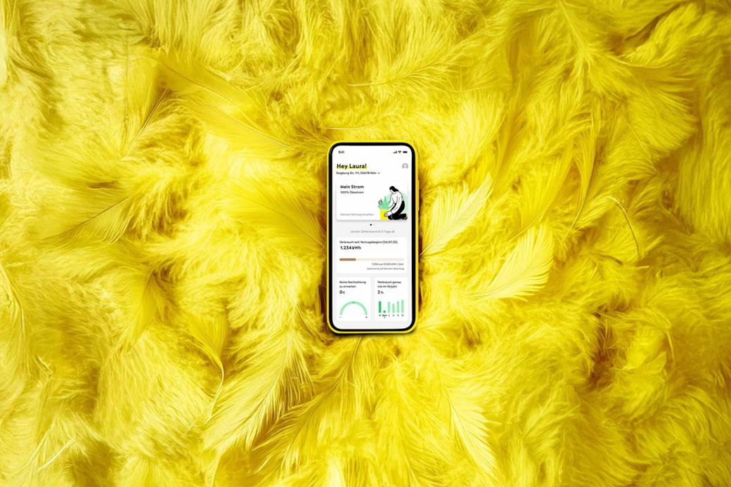 Handy, das die Yello App mit dem Yello Mein Strom Tarif zeigt auf gelben Federn - KI generiert