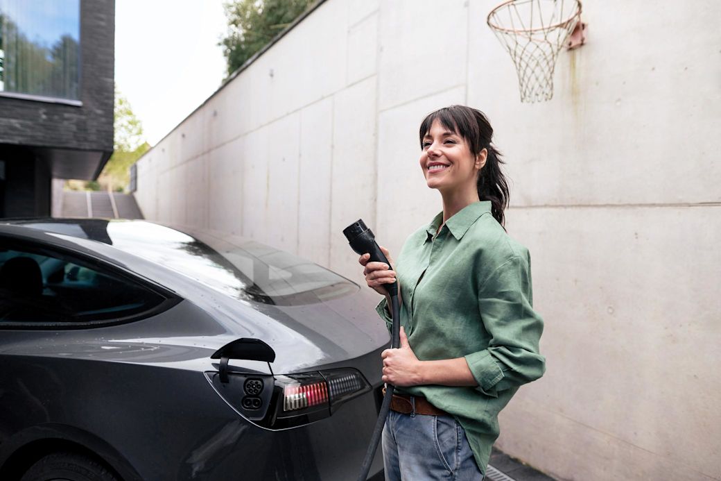 Frau lädt ihr E-Auto zuhause mit Basketballkorb im Hintergrund