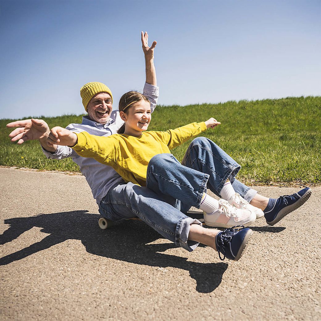 Vater und Tochter sitzen zusammen auf einem Skateboard und fahren den Berg lachend herunter