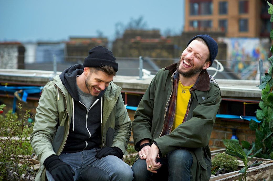 Freunde sitzen im Park, tragen Winter Kleidung und lachen zusammen