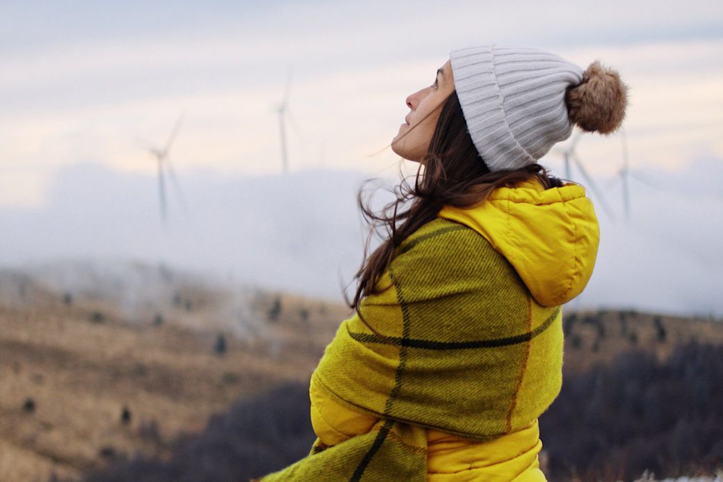 Frau in gelber Winterjacke schaut an einem kalten Tag auf Windkraftanlagen im Hintergrund