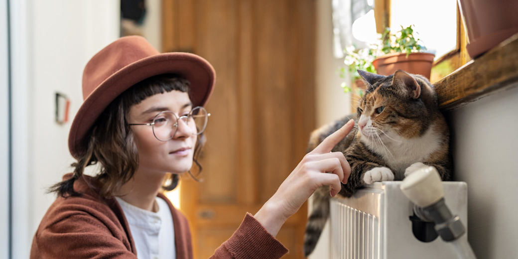 Frau streichelt ihre Katze, die auf der Heizung liegt.
