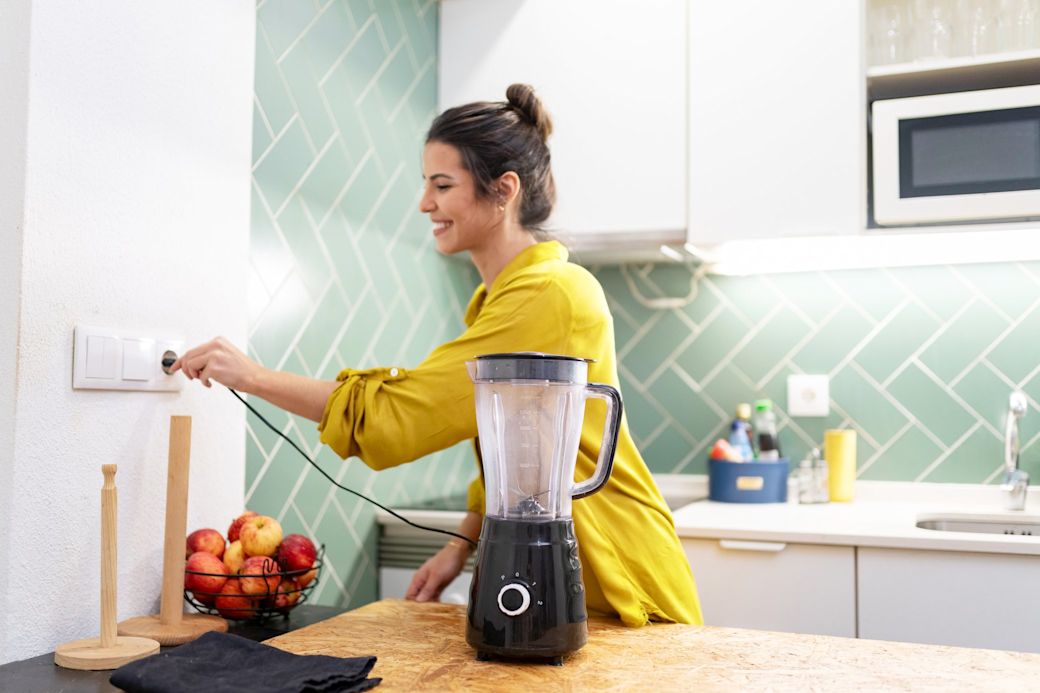 Frau steckt einen Mixer in die Steckdose in der Küche
