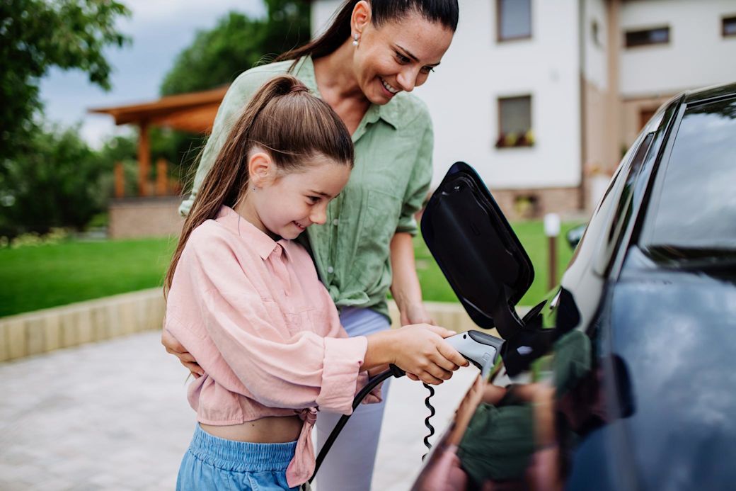 Frau mit kleinem Mädchen laden zusammen ein E-Auto.