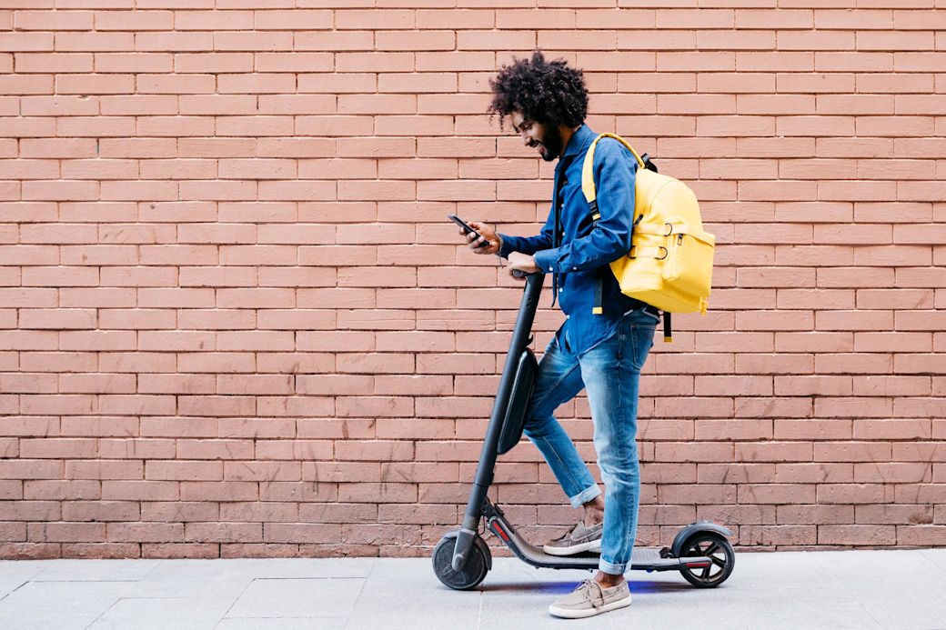 Mann mit E-Scooter schaut aufs Smartphone