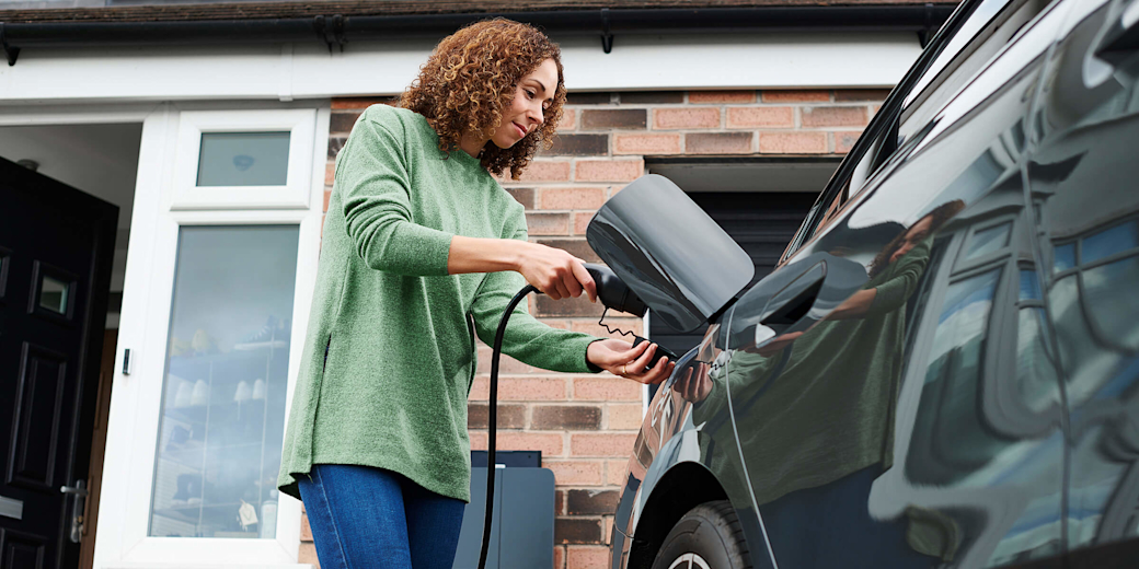 Frau hängt das Ladekabel für E-Auto über die Wallbox.