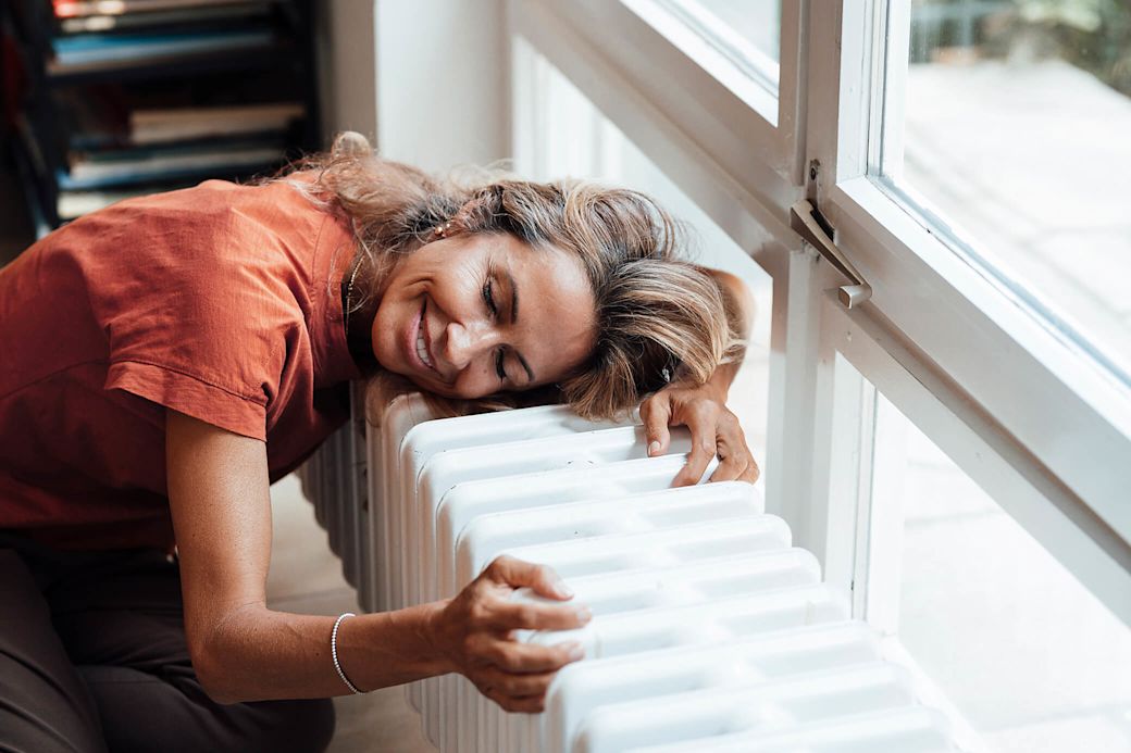 Frau am Fenster schmiegt sich an einen Heizkörper