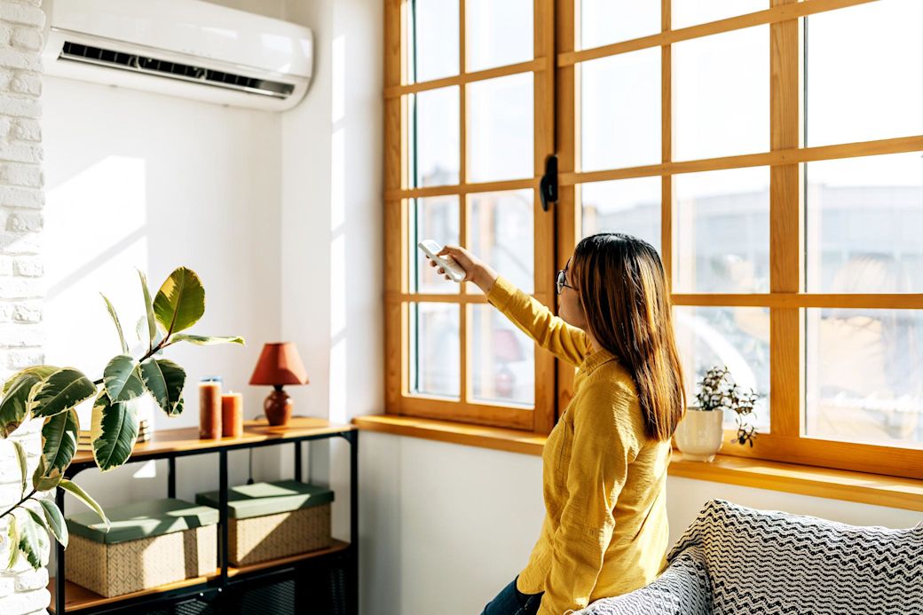 Eine Frau hält eine Fernbedienung in der Hand und schaltet damit ein Klimagerät an. 