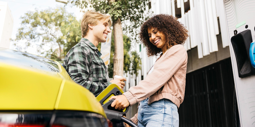 Junges Paar lädt lachend ihr gelbes E-Auto in der Stadt auf