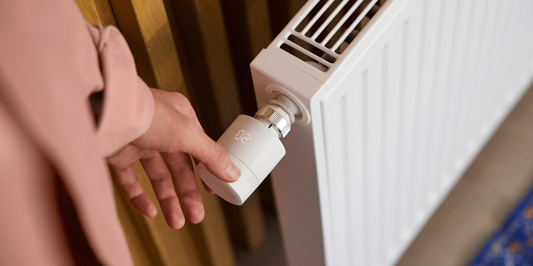 Frau dreht am Thermostat der Heizung.