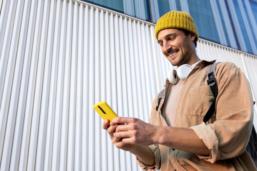 Mann mit gelber Mütze und Kopfköhrern schaut auf ein gelbes Handy in seinen Händen