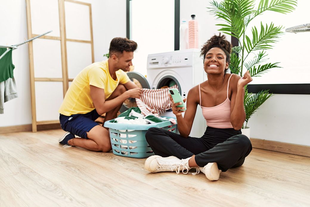 Junges Paar sitzt vor der Waschmaschine und macht zusammen Wäsche
