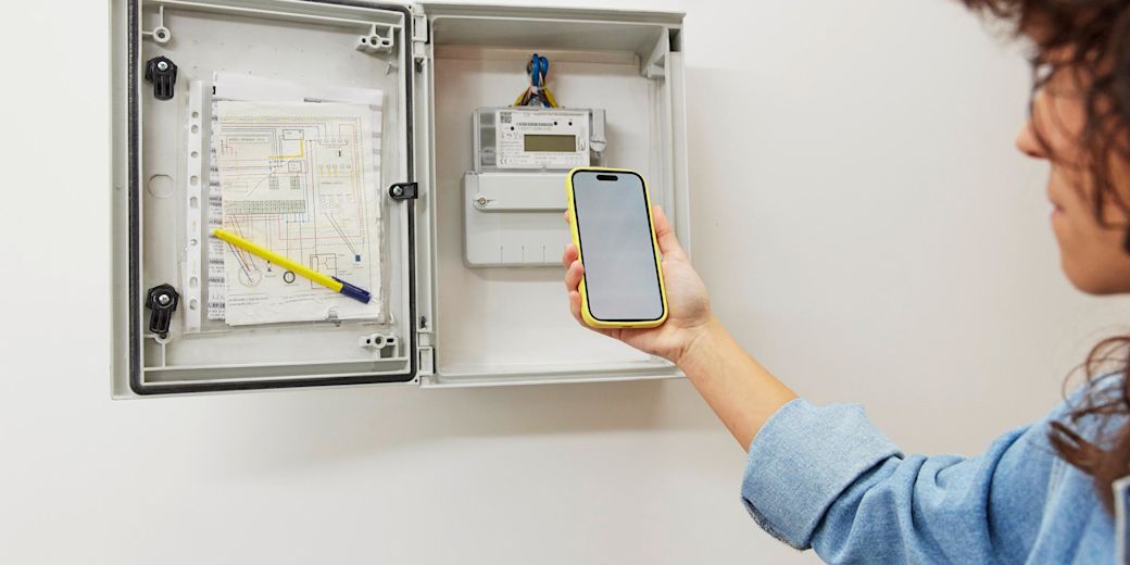 Frau liest mit gelbem Handy in der ihren Stromzähler ab