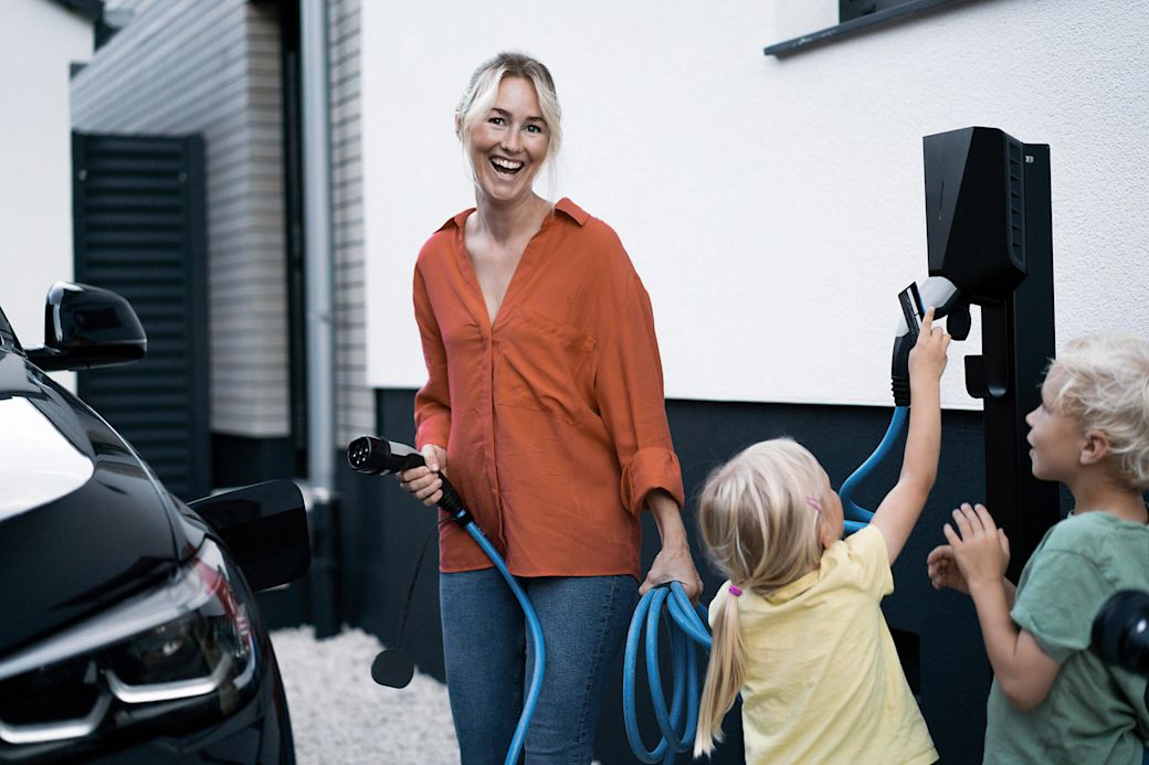 Frau mit zwei Kindern lädt lachend ihr E-Auto mit Wallbox.