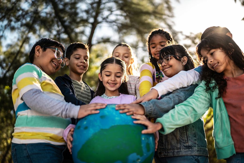 Kinder stehen im Kreis und berühren lächelnd eine Erde aus Pappe