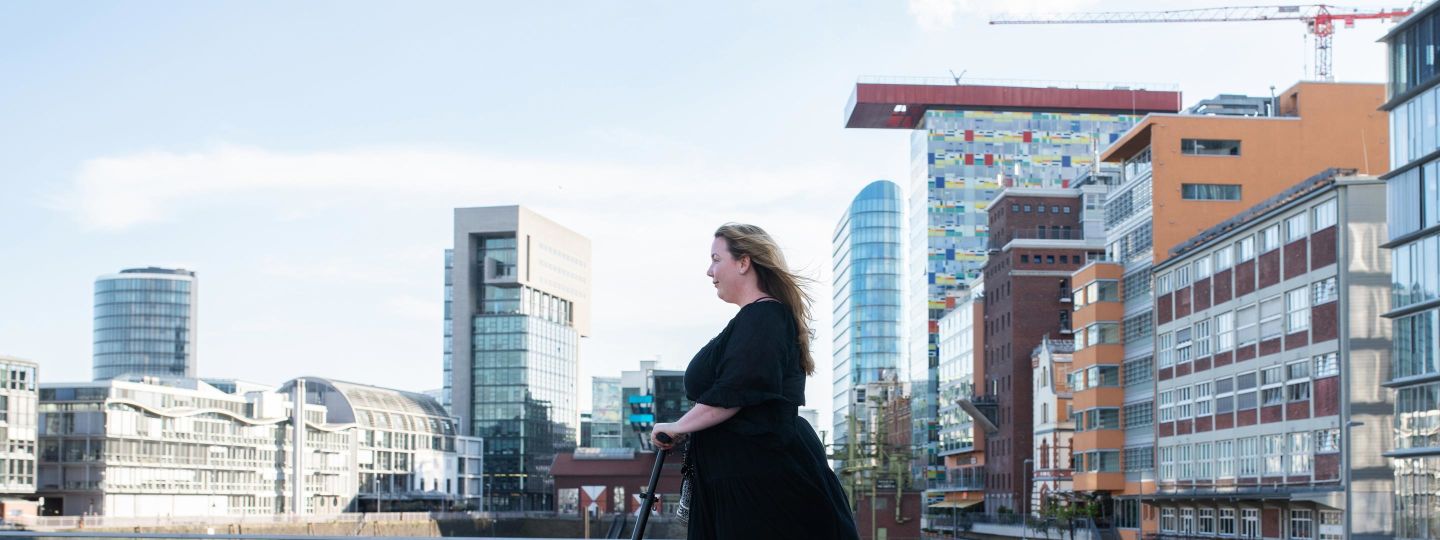 Frau mit schwarzem Kleid rollt auf E-Scooter durch den Rheinhafen in Düsseldorf