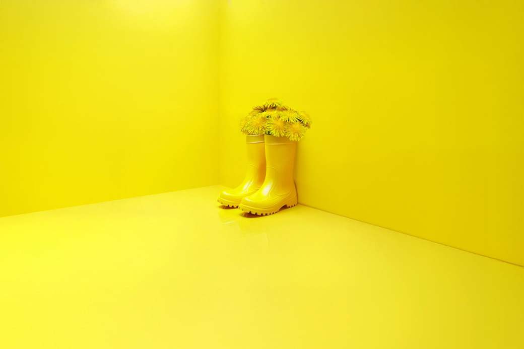 Gelber Raum mit Gummistiefel in denen Blumen stecken - KI Generiert