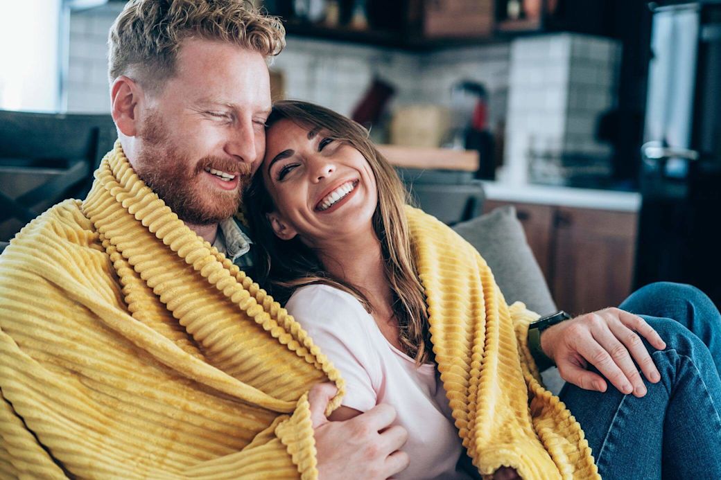 Mann und Frau sitzen auf der Couch eingekuschelt in eine Decke.