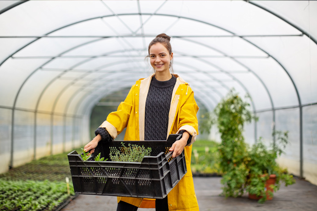 Junge Frau in gelber Regenjacke im Gewächshaus im landwirtschaftlichen Betrieb