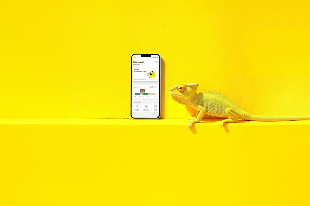 Gelbes Chamäleon schaut auf ein Handy mit Yello App - KI generiert