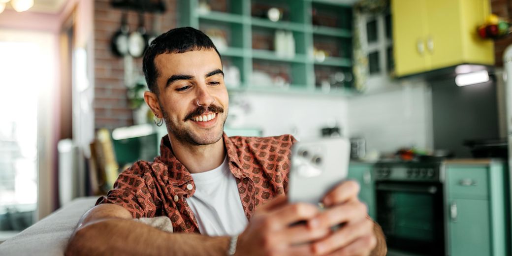 Lächelnder Mann sitzt auf dem Sofa und checkt auf dem Smartphone seinen Energieverbrauch