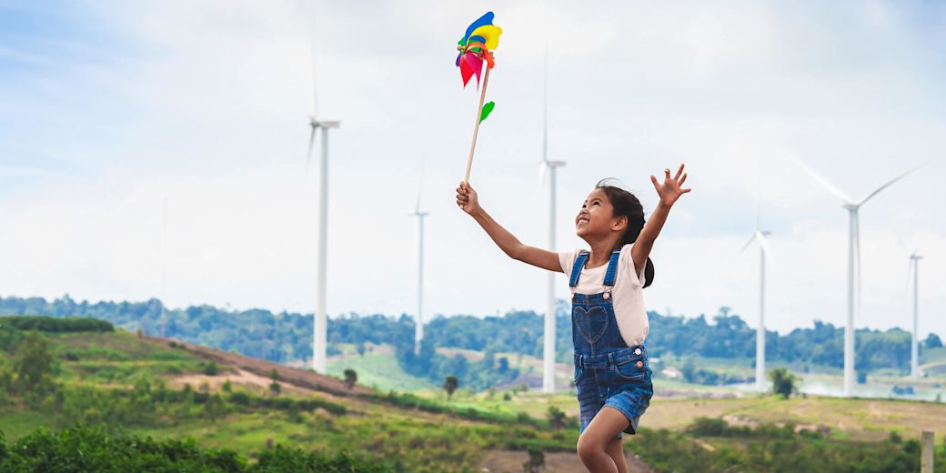 Mädchen läuft mit buntem Windrad durch einen Windpark.