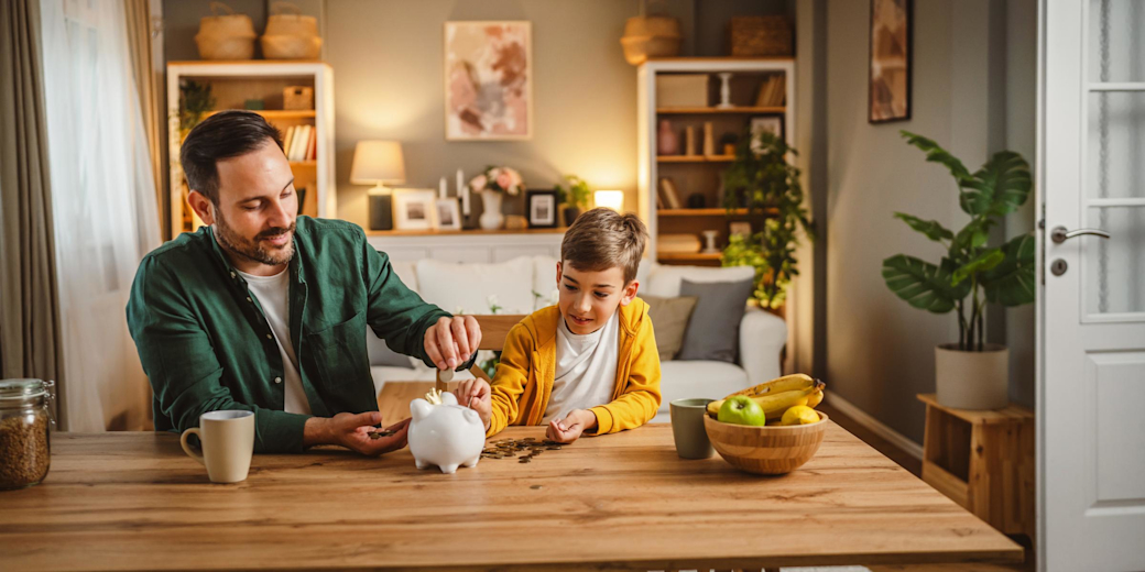 Vater und Sohn sitzen am Tisch im Wohnzimmer und füllen Sparschwein auf