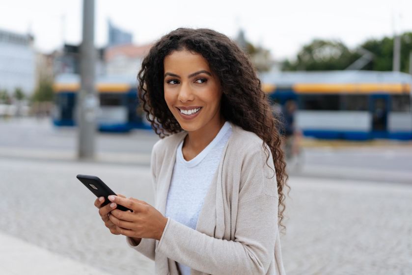 Lachende Frau vor der Leipziger U-Bahn mit Blick auf ihr Smartphone