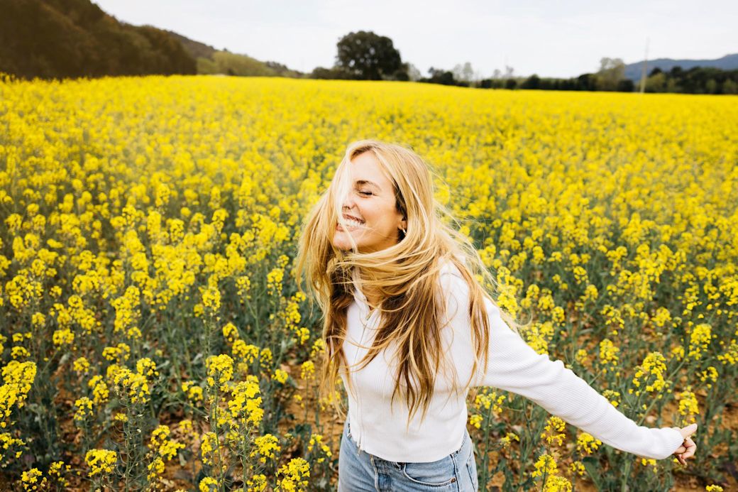 Fröhliche Frau mit langen blonden Haaren tanzt durch gelbes Rapsfeld