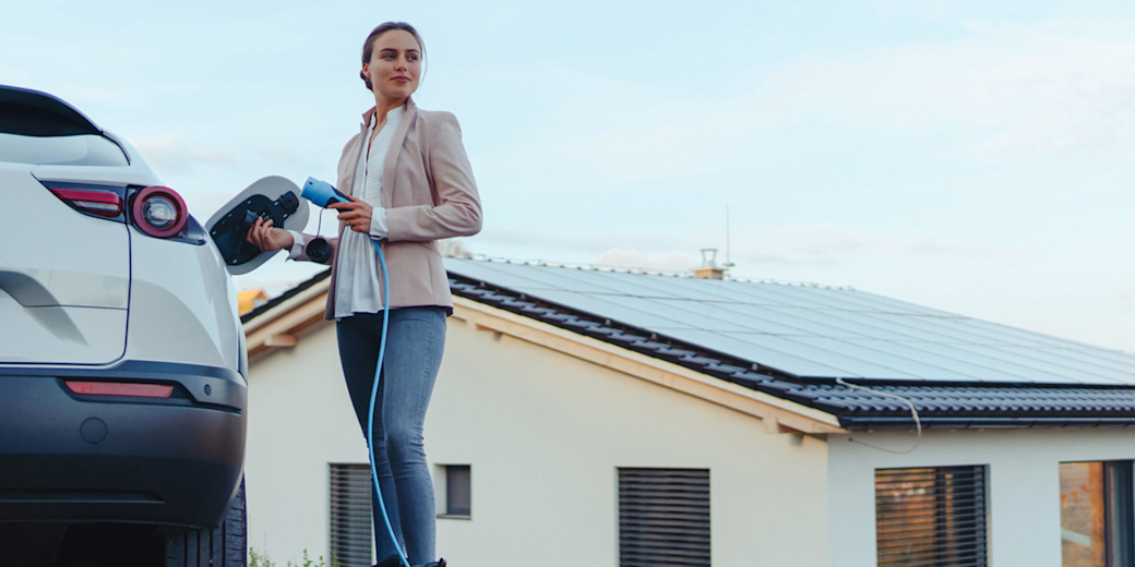 Frau lädt ihr E-Auto - mit eigener Solaranlage auf dem Dach.