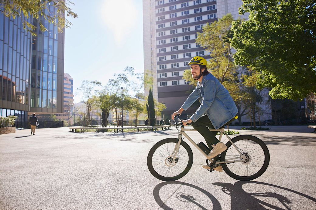 Junger Mann in Jeansjacke fährt mit dem E-Fahrrad durch die Stadt