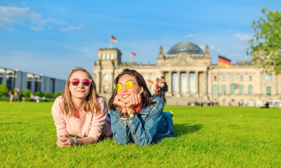 Zwei Frauen liegen vor dem Reichstagsgebäude in Berlin auf der Wiese