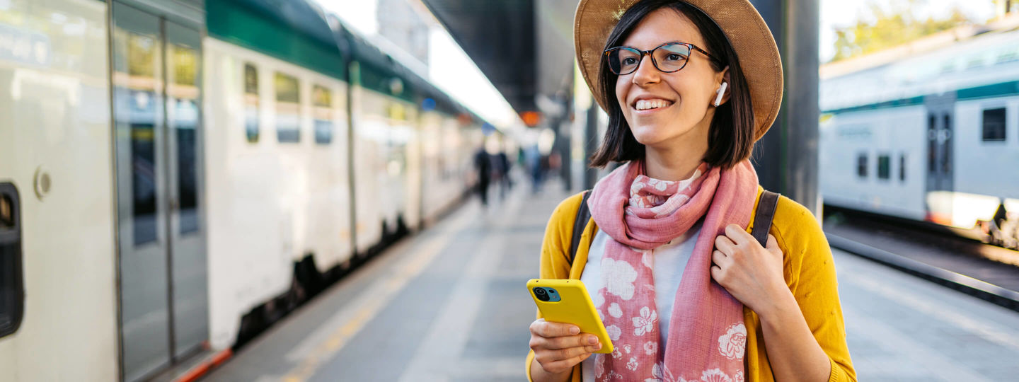 Junge Frau mit gelbem Handy wartet am Bahnhof
