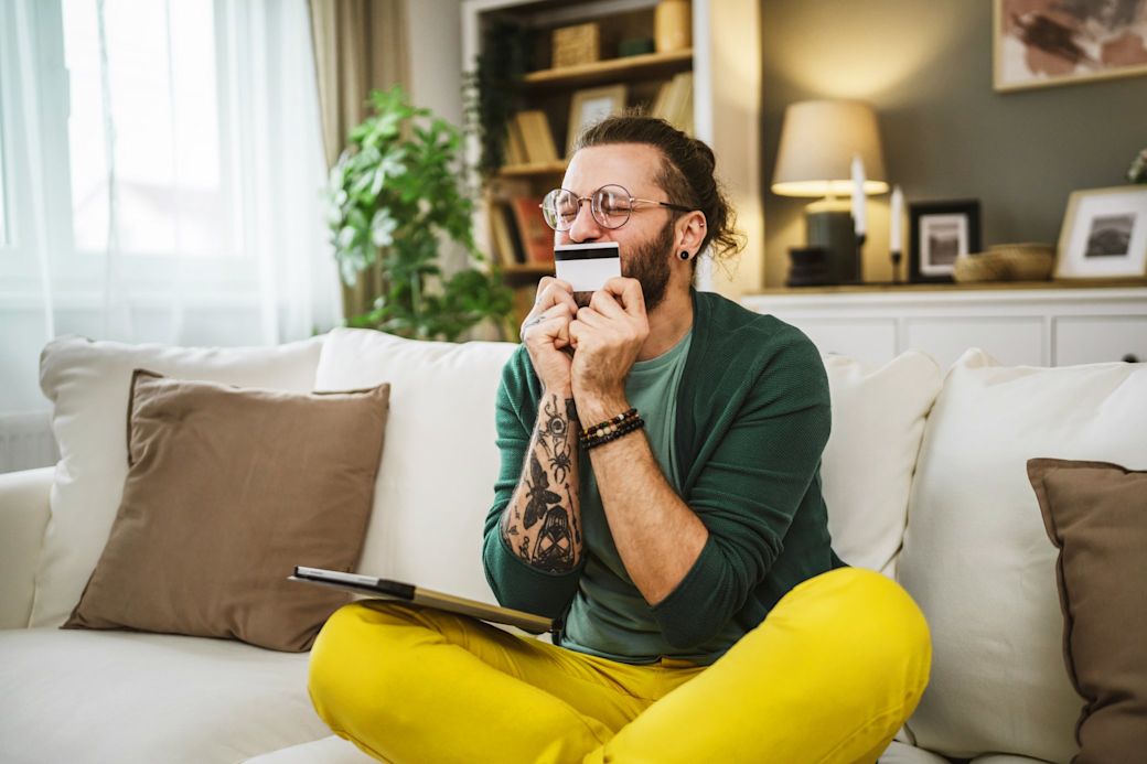Foto von einem jungen Mann, der auf dem Sofa sitzt und seine Kreditkarte küsst.