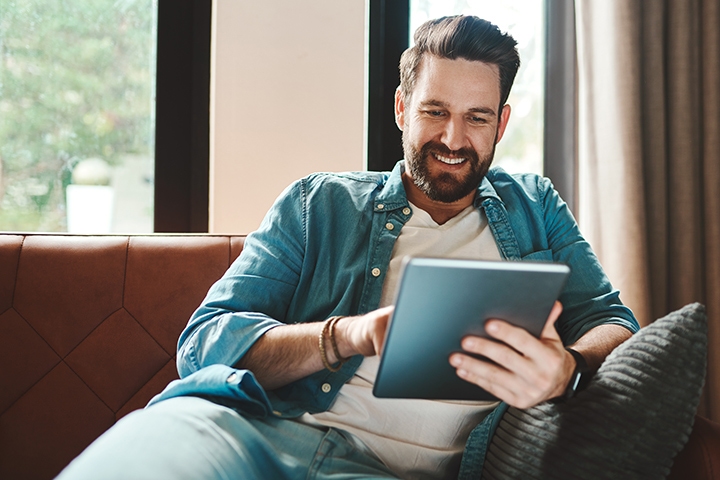 man sitting on his couch looking at his tablet