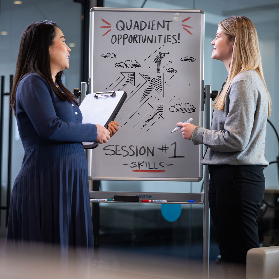 Two women in business attire stand beside a whiteboard displaying Quadient Opportunities Session 1 Skills with arrows.
