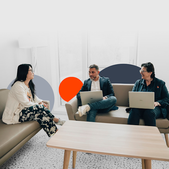 Trois collèges Quadient collaborant sur des ordinateurs portables dans un salon de bureaux moderne avec des sièges beiges et des œuvres murales géométriques colorées.
