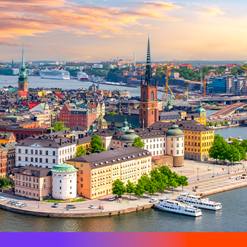 Aerial view of Stockholm's colorful historic buildings and church spires along the waterfront at sunset with orange sky.