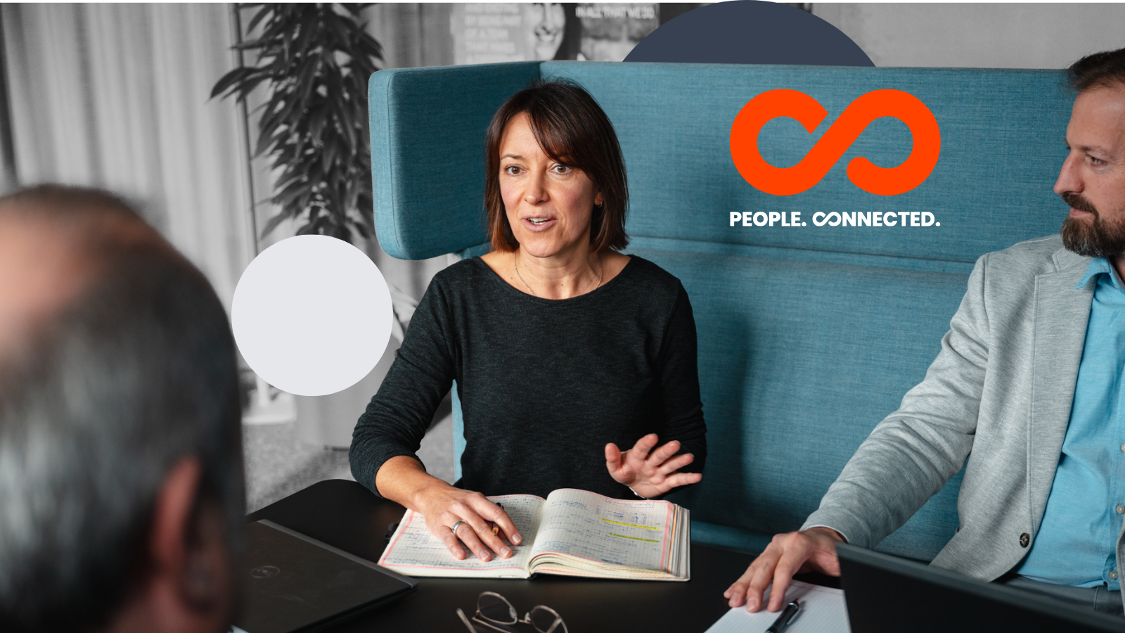 Woman in black shirt gestures while speaking to colleagues on teal sofa with orange infinity logo and People Connected text.