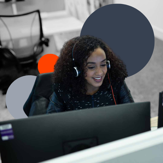 Woman with a headset smiling at her computer screen in a professional office environment