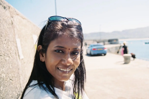 femme souriante dans un paysage côtier, lunettes de soleil sur le dessus de la tête