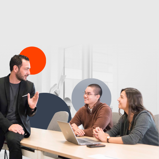 Trois professionnels diversifiés collaborant autour d’une table avec des ordinateurs portables dans un bureau moderne aux motifs muraux circulaires colorés.