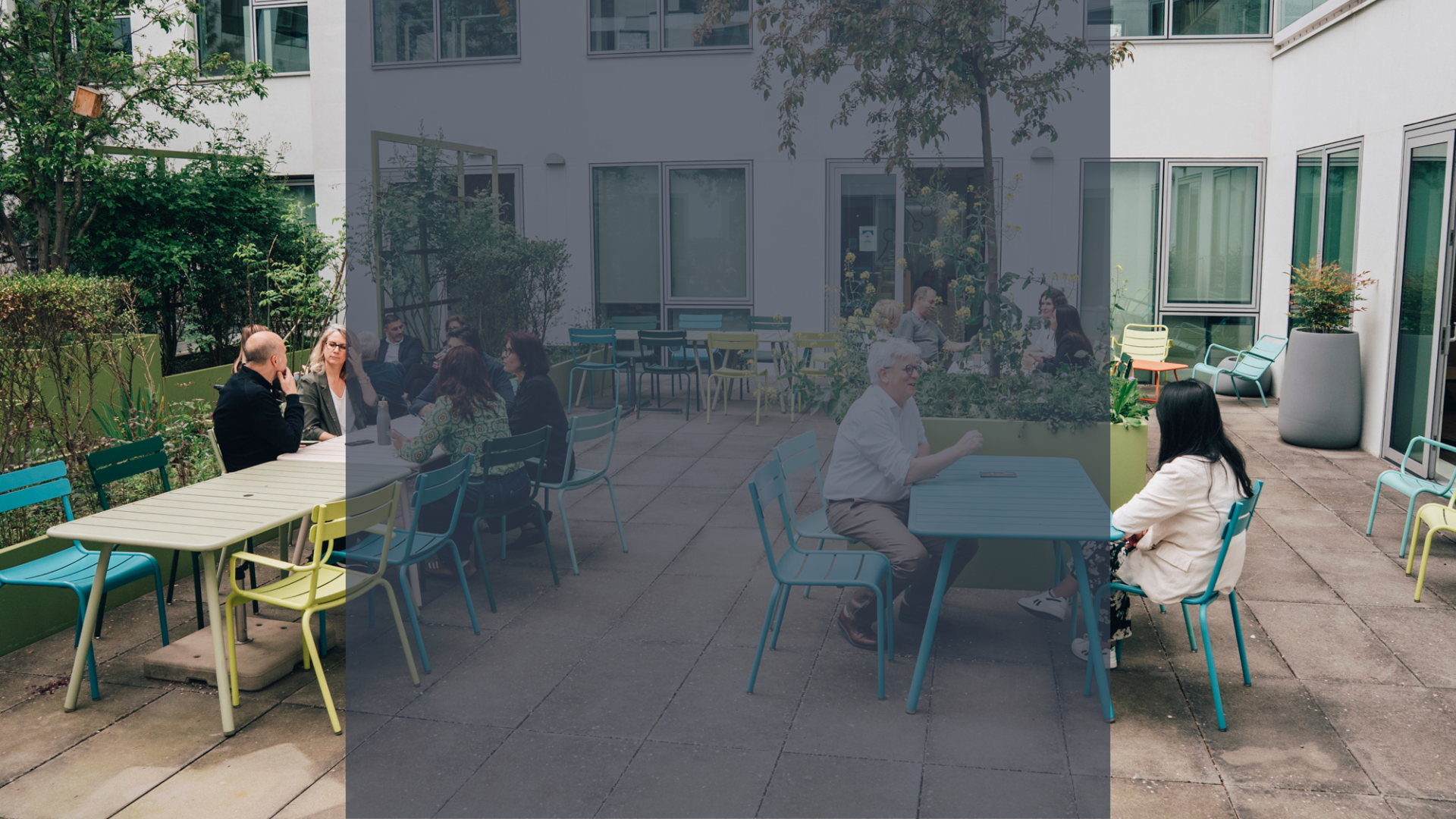 People sitting at colorful outdoor tables in a modern courtyard patio surrounded by buildings and greenery.