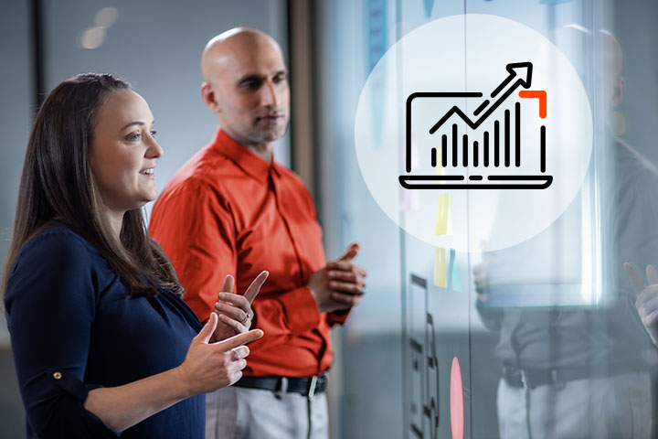 Two business professionals viewing a laptop icon with upward trending graph and arrow displayed on a transparent screen