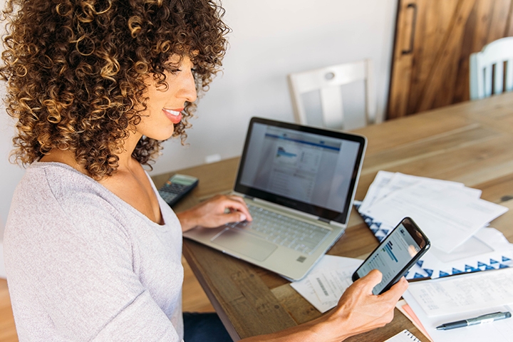woman sits at a table with laptop, financial reports and phone