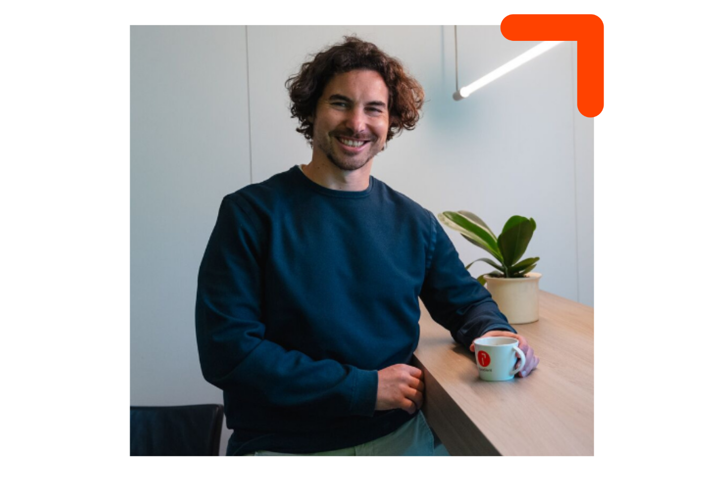 un jeune homme tenant une tasse avec le logo Quadient et portant un chandail bleu foncé, souriant en regardant à droite