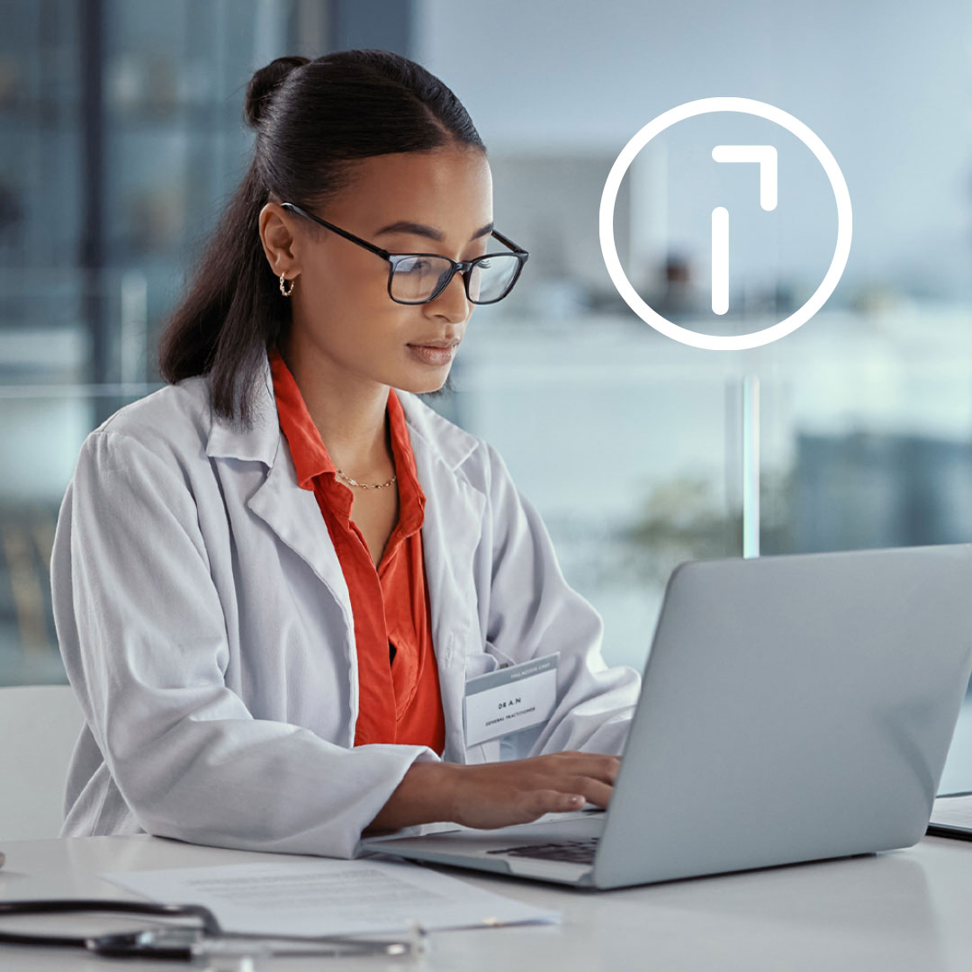 Female healthcare professional in white lab coat and orange shirt wearing glasses working on laptop with cane icon overlay.