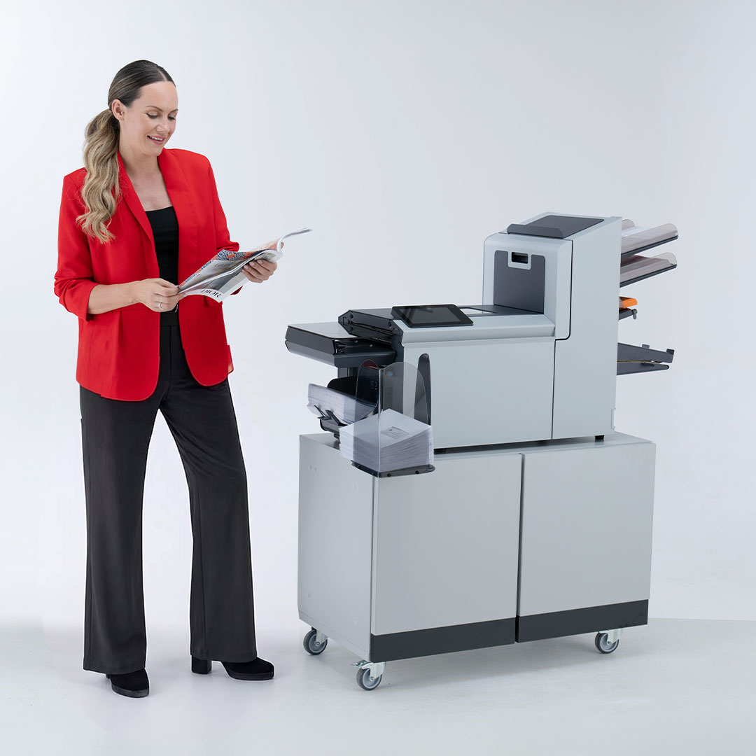 Woman in red blazer and black outfit reviewing documents beside a DS-77 Folder inserter mail processing machine on a wheeled cart.