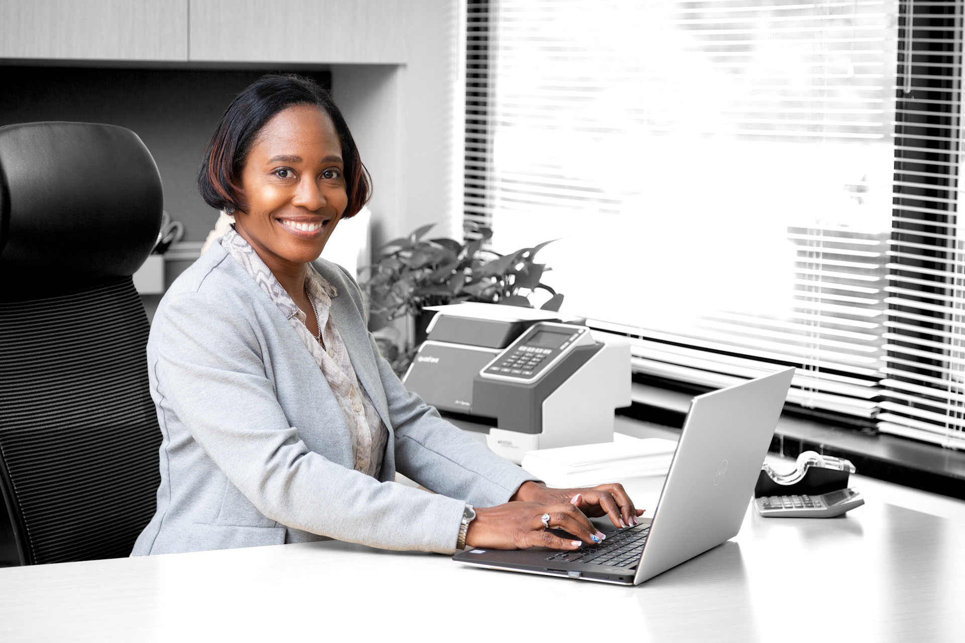 Woman working on a laptop at an office desk near a franking machine.