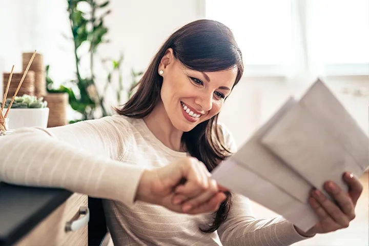 Smiling woman in orange shirt with glasses sitting at desk next to postage meter machine with stamp icon overlay